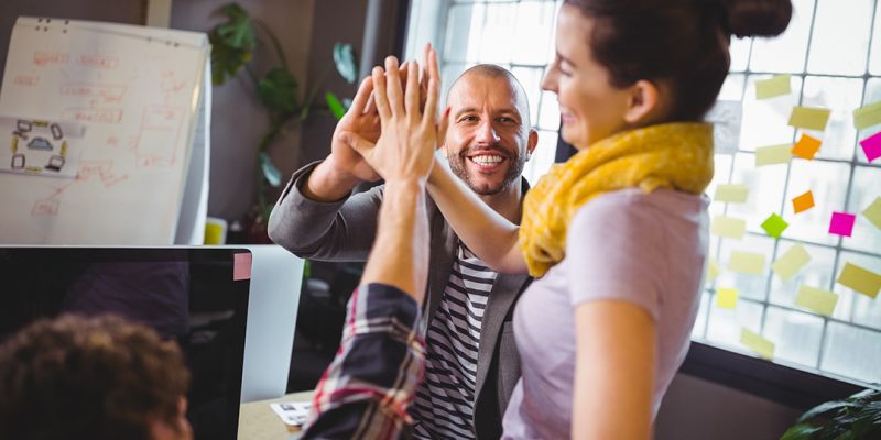 Cheerful coworkers high fiving in creative office